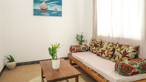 A living room with a wooden sofa, patterned cushions, a painting of sailboats, a potted plant, and a small table. - Hiliki Holiday Home Paje - by Liv Zanzibar (Paje)