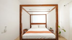 A four-poster bed with white bedding and an orange throw blanket, a small bedside table with a book and a vase of flowers, and a potted plant on the floor. - Hiliki Holiday Home Paje - by Liv Zanzibar (Paje)