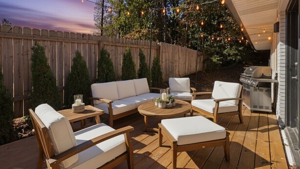 Een houten terras met buitenmeubilair, sfeerverlichting en een barbecue.