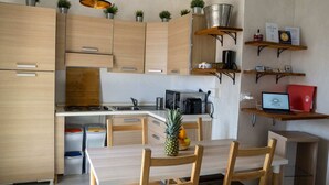 Una cocina moderna con armarios de madera, una mesa de comedor con sillas, una computadora portátil en un estante y una pequeña planta en la encimera.