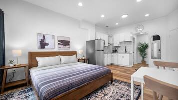 Una habitación de hotel moderna con una cama de madera, un escritorio pequeño, una mesa de comedor y una kitchenette.