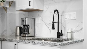 Een keuken met een granieten aanrecht, een koffiezetapparaat, een zwarte kraan en een witte zeepdispenser.