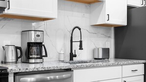 Eine moderne Küche mit weißen Schränken, einem Edelstahl-Geschirrspüler, einer Kaffeemaschine und einem schwarzen Wasserhahn.