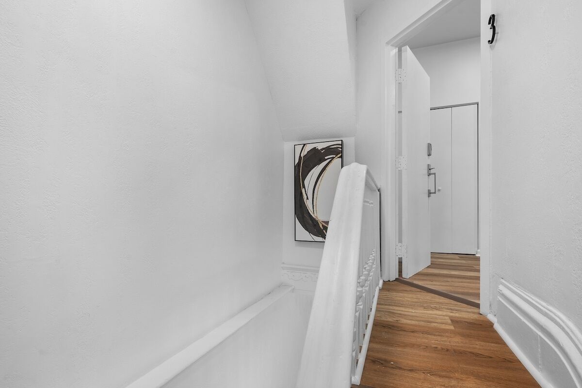 A hallway with white walls, a wooden floor, and a door marked with the number 3.