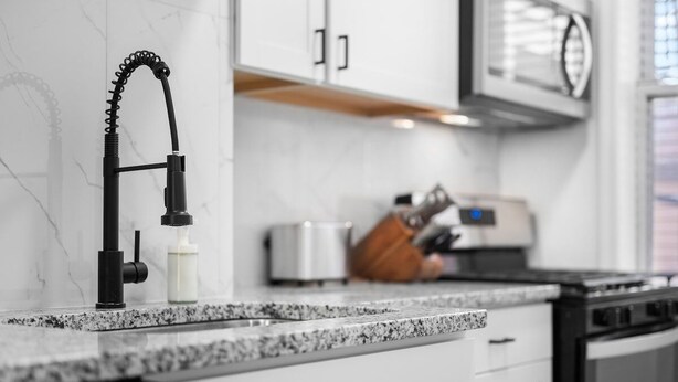 A modern kitchen with a granite countertop, a black faucet, and white cabinetry.