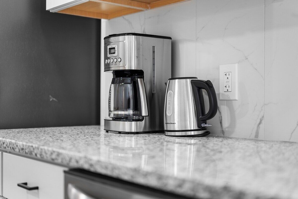 A kitchen with a coffee maker and a kettle on a marble countertop.