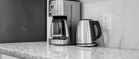 A kitchen with a coffee maker and a kettle on a marble countertop.