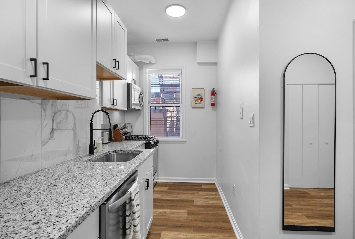 A modern kitchen with white cabinets, a granite countertop, and a wooden floor.