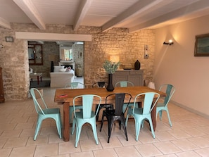 A dining area with a wooden table and chairs, a stone wall, and a view into another room.