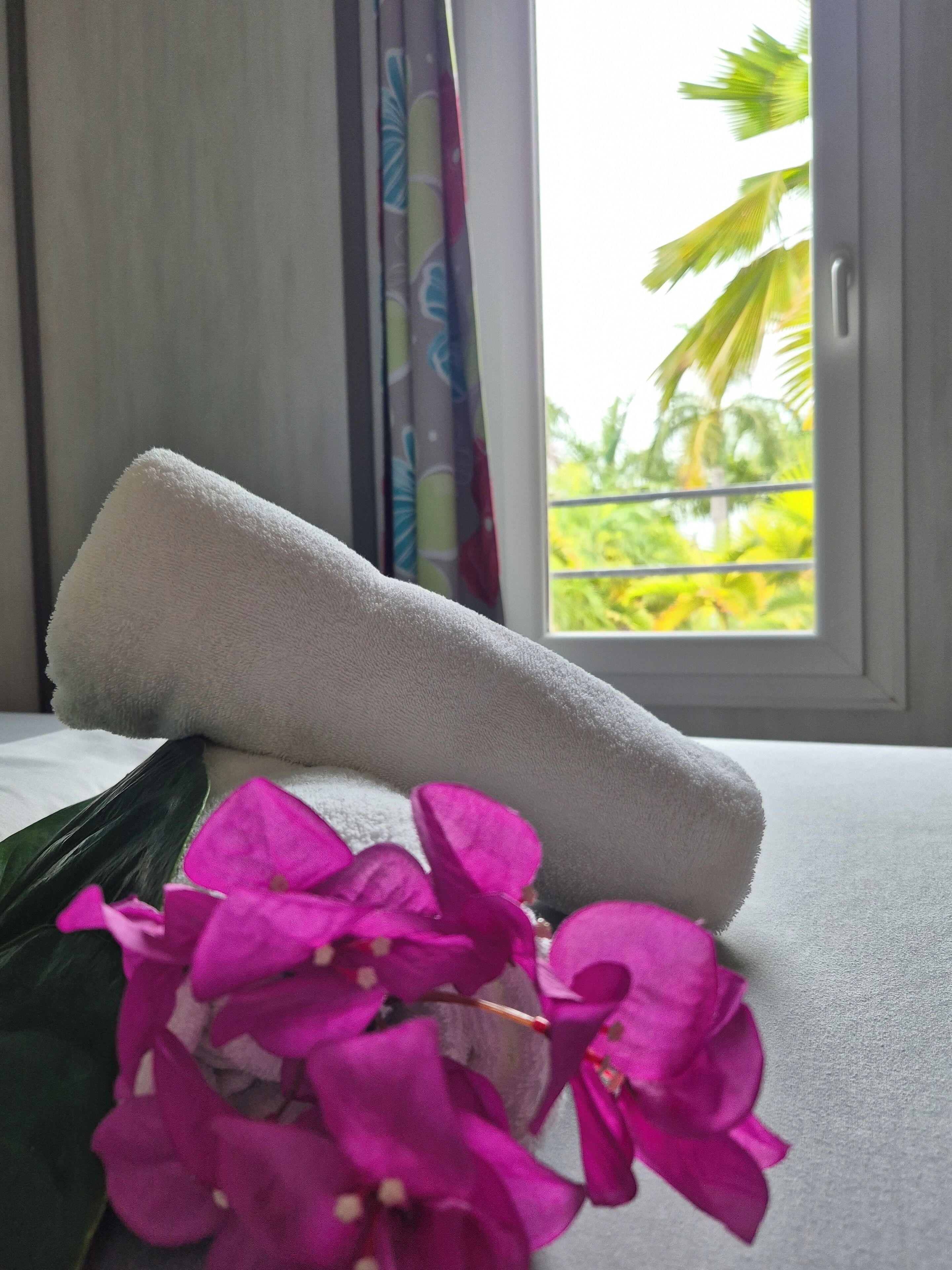A white towel on a bed with a window view of palm trees.