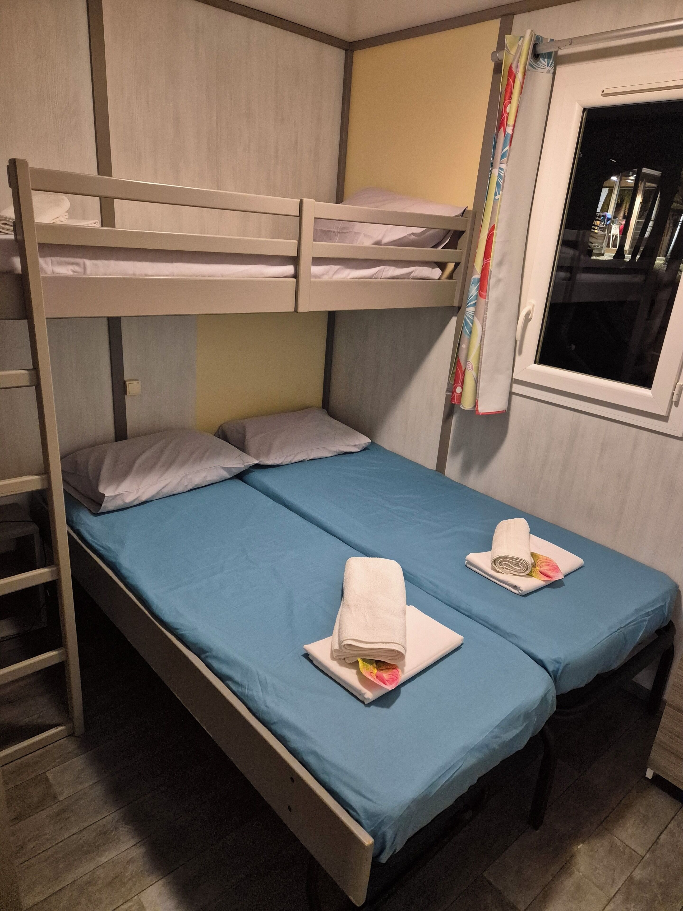 Ein Schlafzimmer mit Etagenbett, zwei Betten, einem Fenster mit Vorhängen und Holzboden.