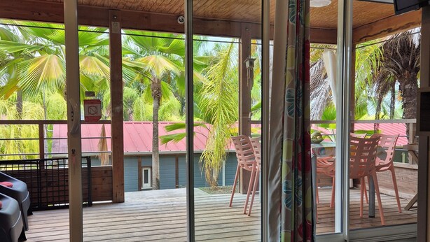 Une pièce dotée d’une porte-fenêtre coulissante donnant sur une terrasse extérieure avec un plancher en bois et du mobilier d’extérieur.