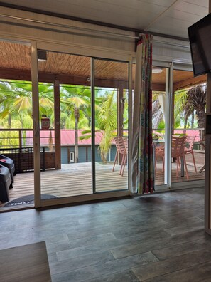 Ein Zimmer mit einer Schiebeglastür, die auf eine Terrasse mit Holzbelag und Gartenmöbeln führt.