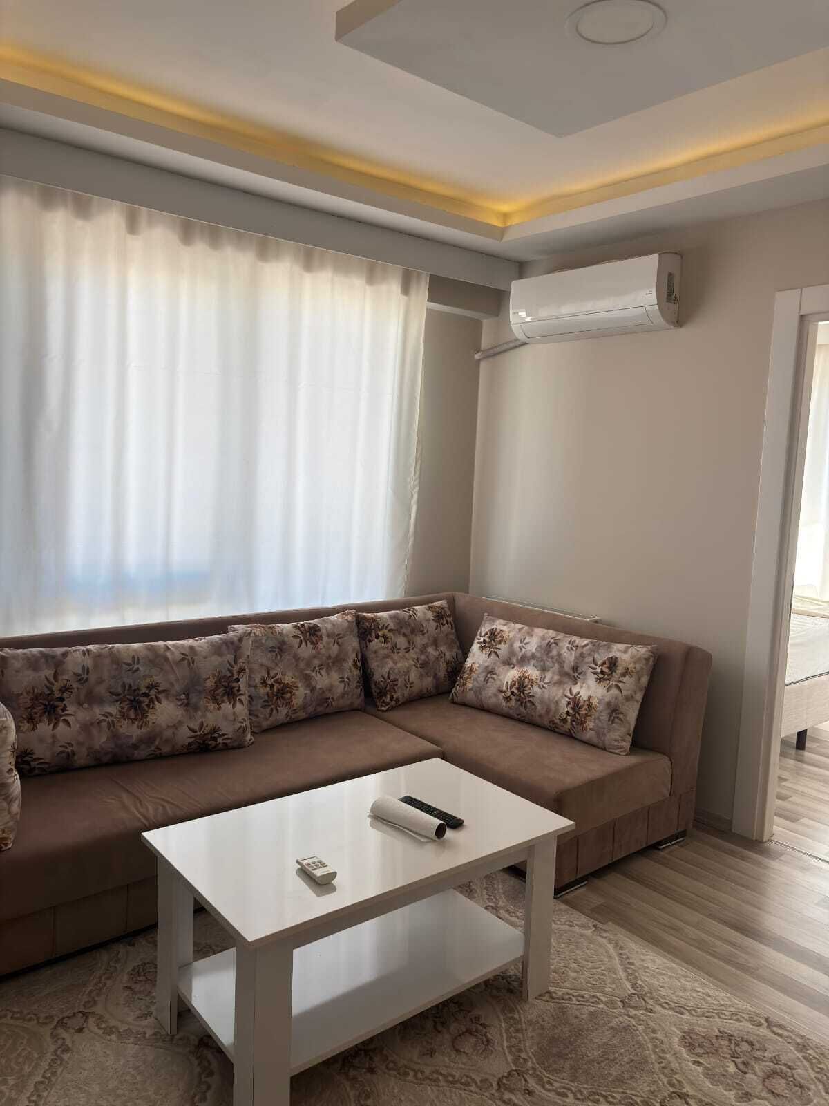 Un soggiorno con un divano color beige, cuscini floreali, un tavolino da caffè bianco e un tappeto decorato.