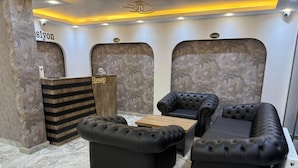 A lobby with a reception desk, two black leather sofas, a wooden coffee table, and marble flooring. - Maraş Blue Life Suite (Kahramanmaras)