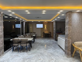 Uma sala de conferências com piso de mármore, mesas, cadeiras e uma tela de projeção.