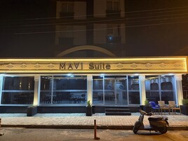 Exterior do hotel Mavi Suite, com várias janelas e uma scooter estacionada em frente.