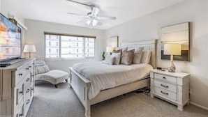 A bedroom with a bed, a nightstand, a dresser, a chair, a ceiling fan, and a large window. - Beautiful Sand Caper 408. 2B/2B condo steps from the Gulf. AMAZING Sunsets (Fort Myers Beach)