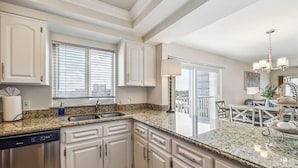 A kitchen with white cabinets, granite countertops, a dishwasher, and a dining area with a chandelier. - Beautiful Sand Caper 408. 2B/2B condo steps from the Gulf. AMAZING Sunsets (Fort Myers Beach)