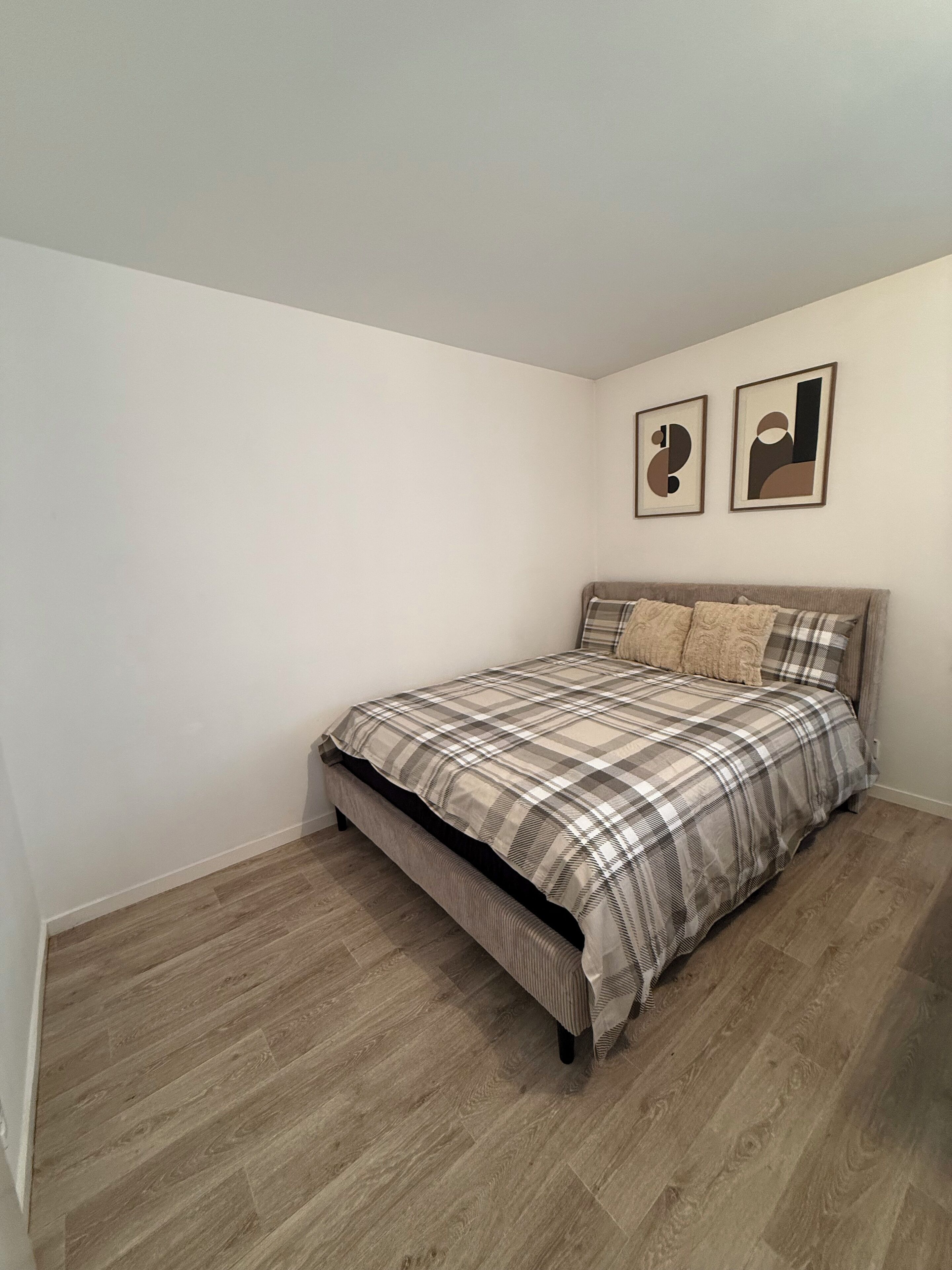 A bedroom with a bed, wooden flooring, and two framed pictures on the wall.