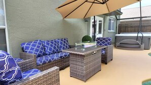 Un espace patio aménagé avec des meubles en osier, une table à plateau en verre et un parasol beige.