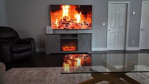 Un salon moderne avec un téléviseur à écran plat fixé au-dessus d’une cheminée, une table basse en verre et un canapé en cuir.