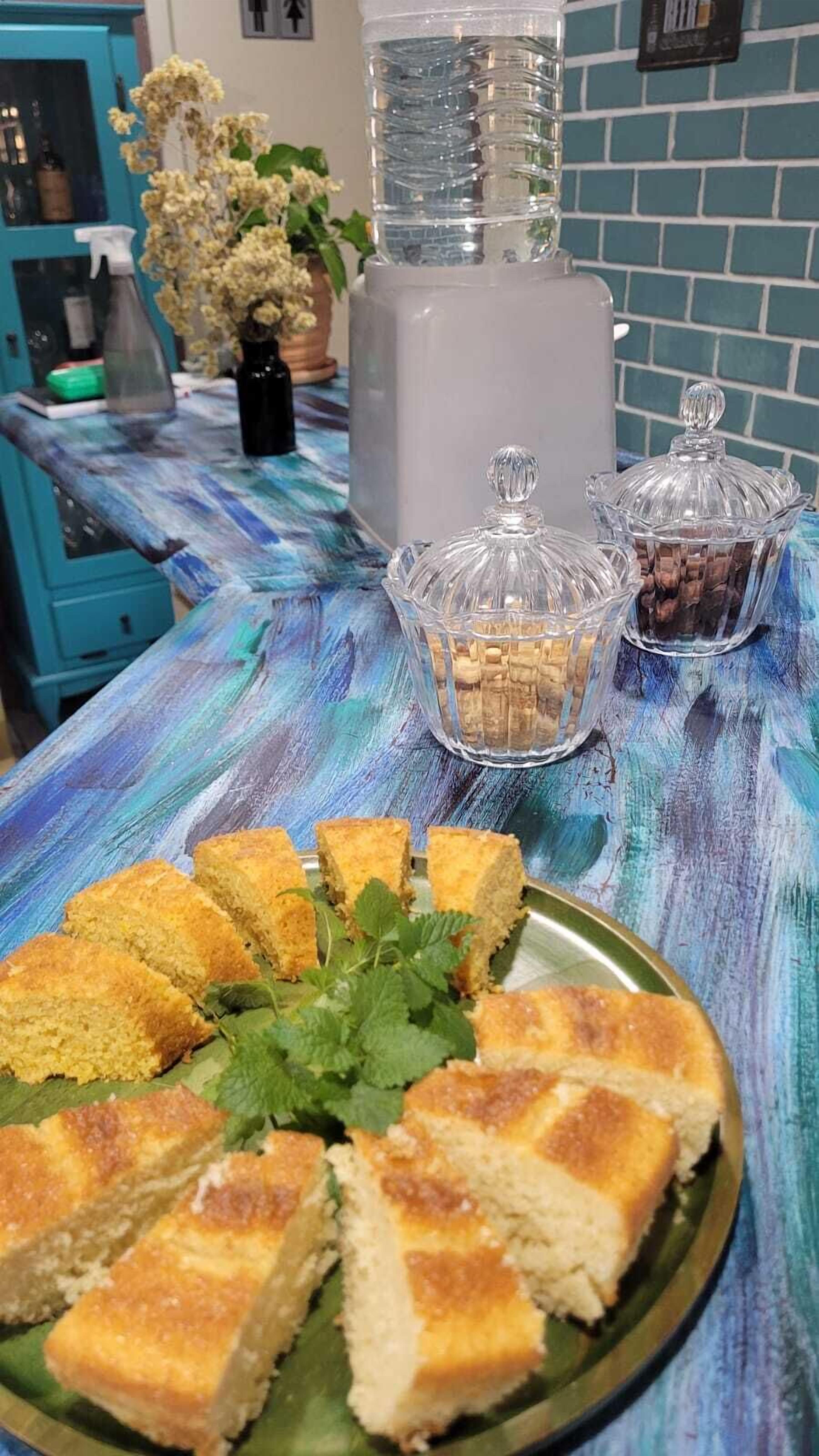 Una mesa con mantel azul y blanco, un plato de pan y dos recipientes de vidrio con alimentos.
