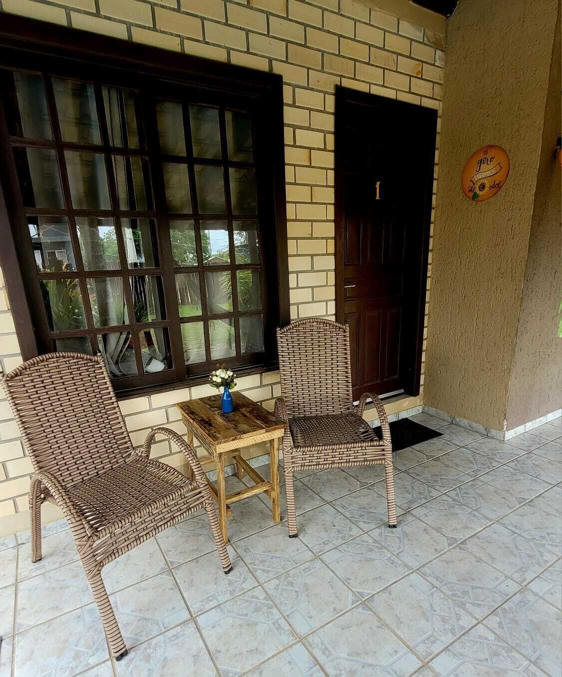 Un patio con mobiliario de mimbre y una mesa, un ventanal grande y una puerta.