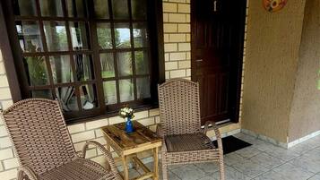 Un patio con mobiliario de mimbre y una mesa, un ventanal grande y una puerta.