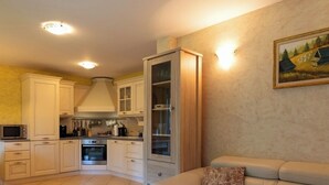 Una cucina moderna con mobili bianchi, forno integrato e microonde. Nell'area soggiorno, un divano beige con un cuscino decorato.