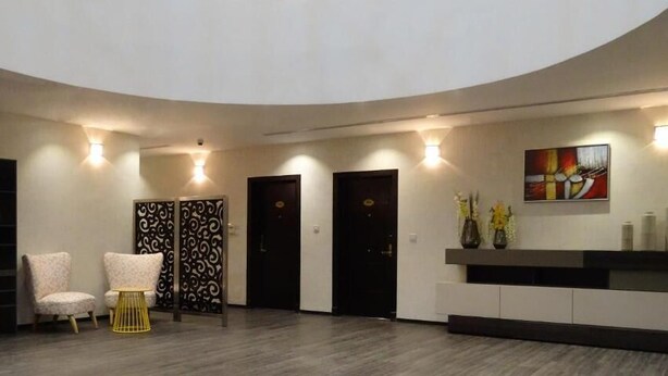 A modern reception area with a curved ceiling, a reception desk, two chairs, a decorative wall piece, and a set of doors. - al sahafah gate hotel (Riyadh)