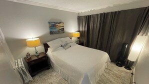 Een hotelkamer met een bed, twee bedlampen, een nachtkastje, een radiator, een raam met gordijnen en een schilderij aan de muur.