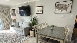 Een woonkamer met een grijze bank, een eettafel met stoelen, een flatscreen televisie aan de muur en een inlijsting kaart van de VS.
