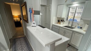 Een moderne keuken met witte kastjes, een centraal eiland en een raam met zonwering.
