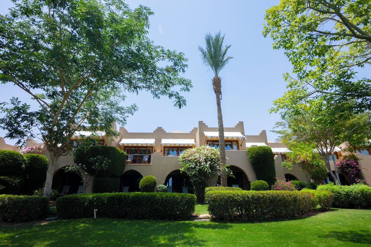 A courtyard with a palm tree, well-manicured hedges, and a building with arched walkways and balconies.