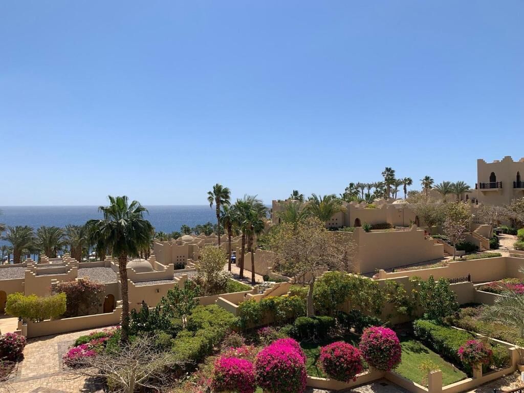 A resort with Mediterranean architecture, palm trees, and a view of the sea.