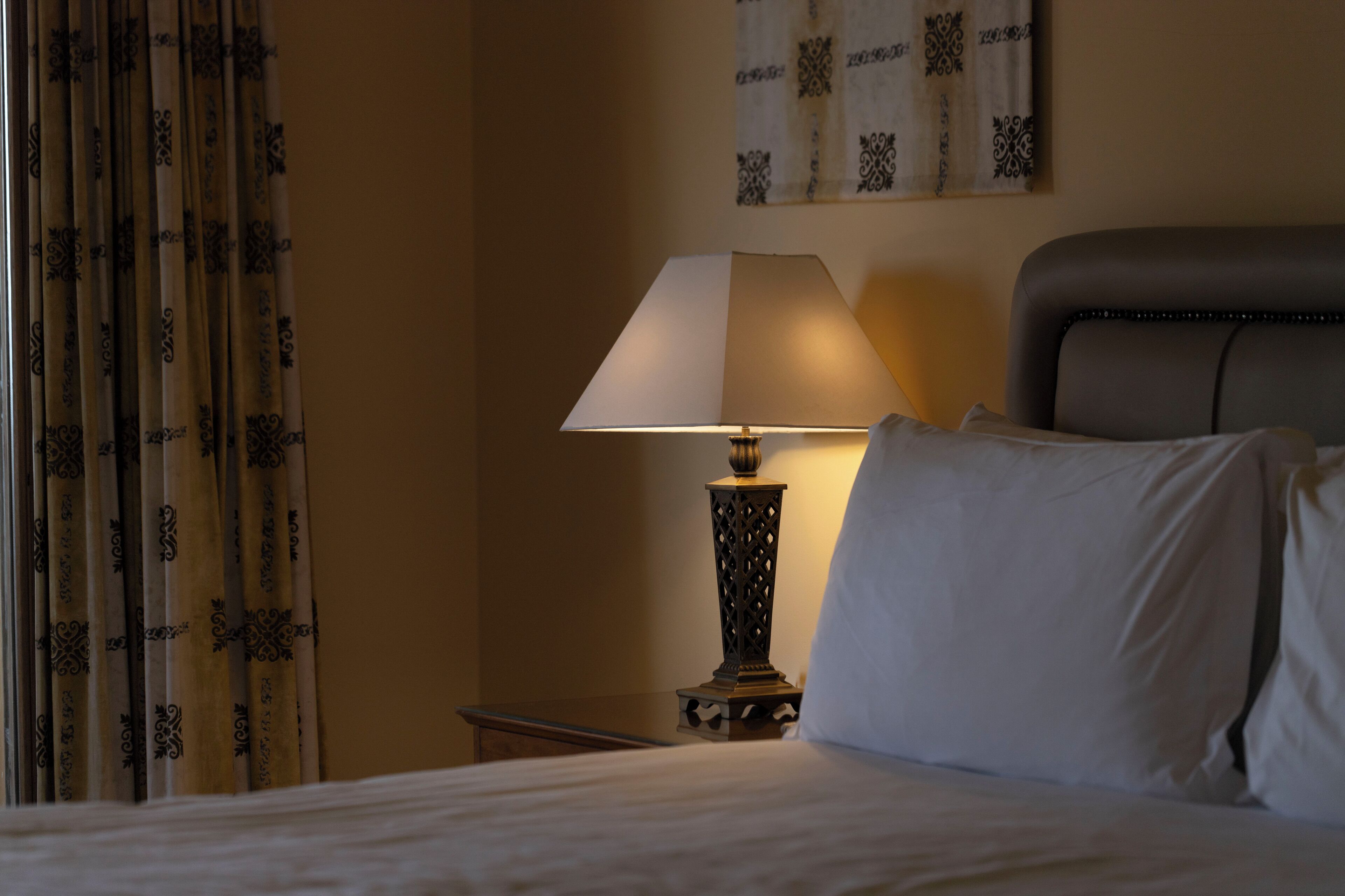 Une chambre d’hôtel avec un lit, une table de chevet, une lampe et un rideau.