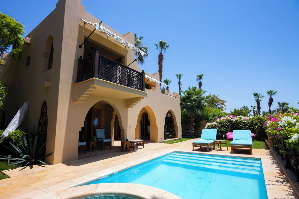 A poolside area with a pool, lounge chairs, and a building with arched doorways and balconies.
