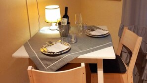 A dining area with a table set for two, a television mounted on the wall, and a vintage poster.