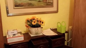 A desk with a painting, a vase with flowers, and some office supplies.