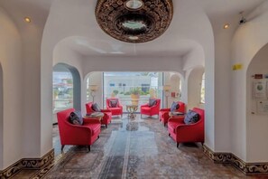 A spacious lobby with red armchairs arranged around a central table, large windows, and a decorative ceiling. - Grand Muthu Oura View Beach Club (Albufeira)