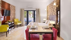 Une chambre d’hôtel comprenant un lit, une télévision, une table à manger avec des chaises, un canapé et une fenêtre avec des rideaux.