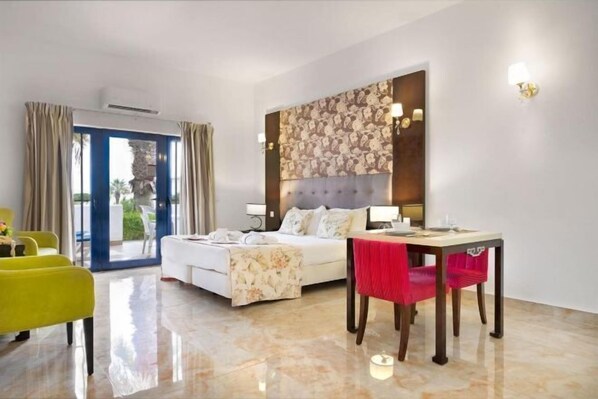 A hotel room with a bed, a dining table, a yellow armchair, and a view of the outdoors.