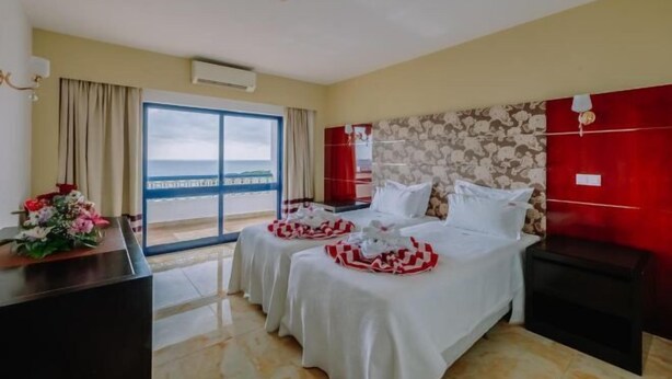 Une chambre d’hôtel avec deux lits, un bureau et vue sur la mer.