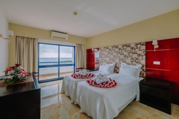 Une chambre d’hôtel avec deux lits, un bureau et vue sur la mer.