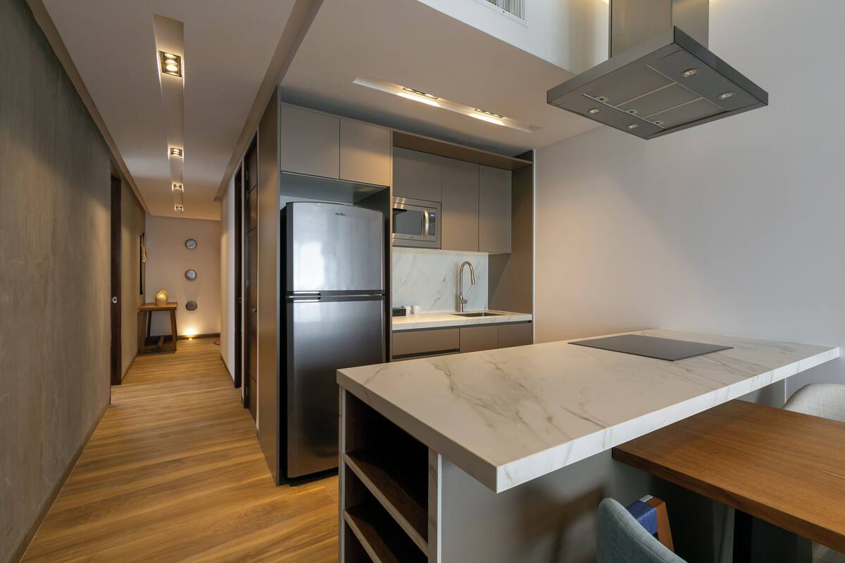 A modern kitchen with a built-in refrigerator, microwave, and sink, featuring a marble countertop and wooden flooring.
