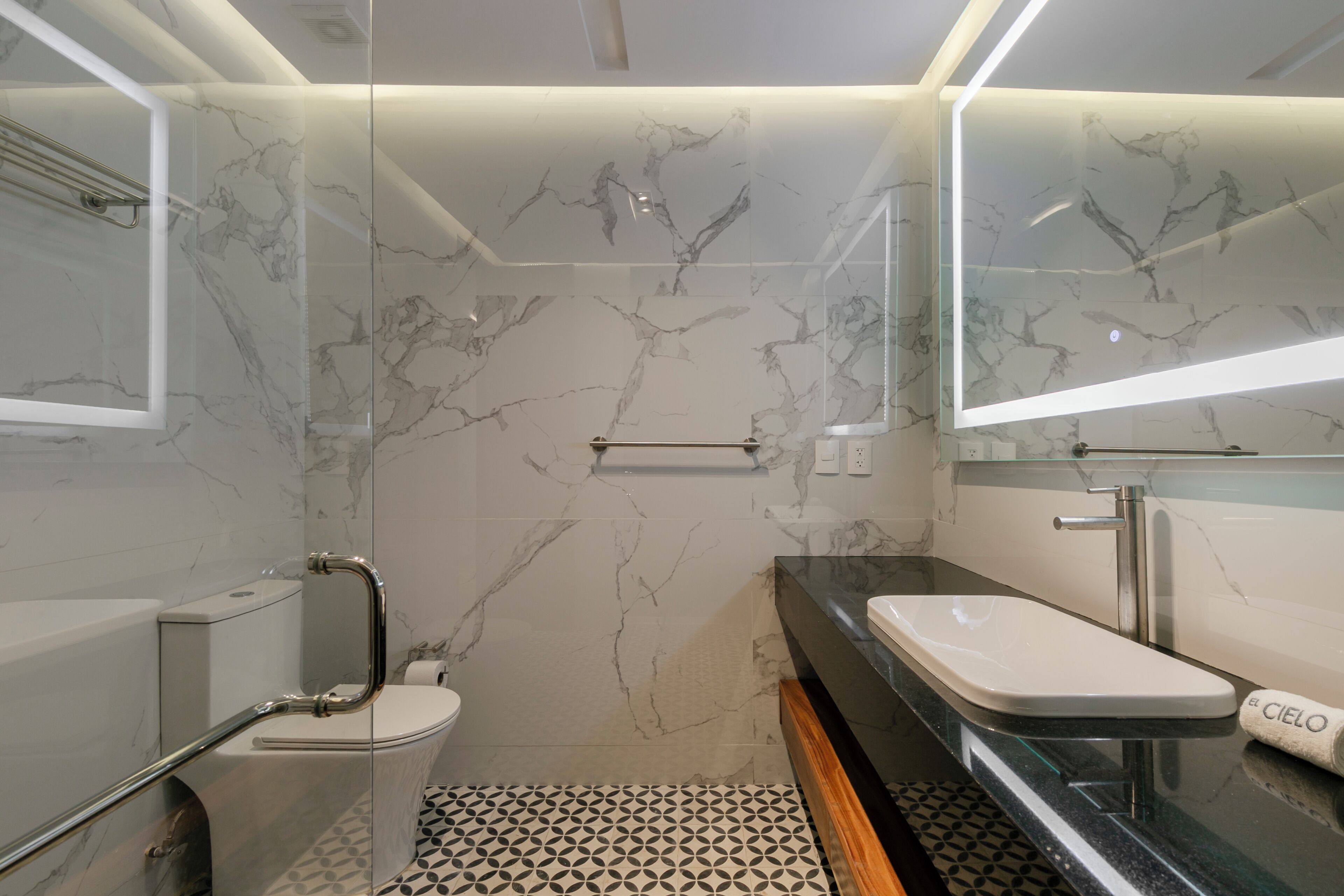 A modern bathroom with a glass shower enclosure, a white toilet, a black sink, and a marble-patterned wall.