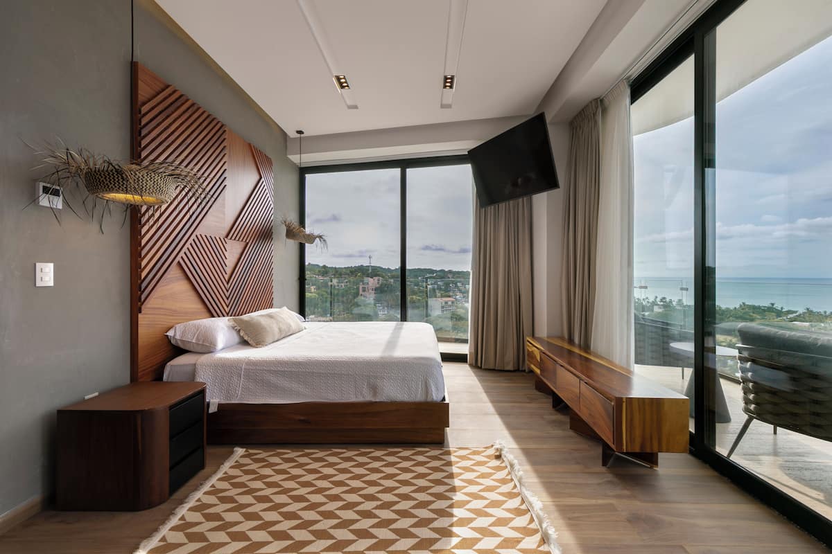 A modern bedroom with a large bed, a view of the city, and a balcony with a view.