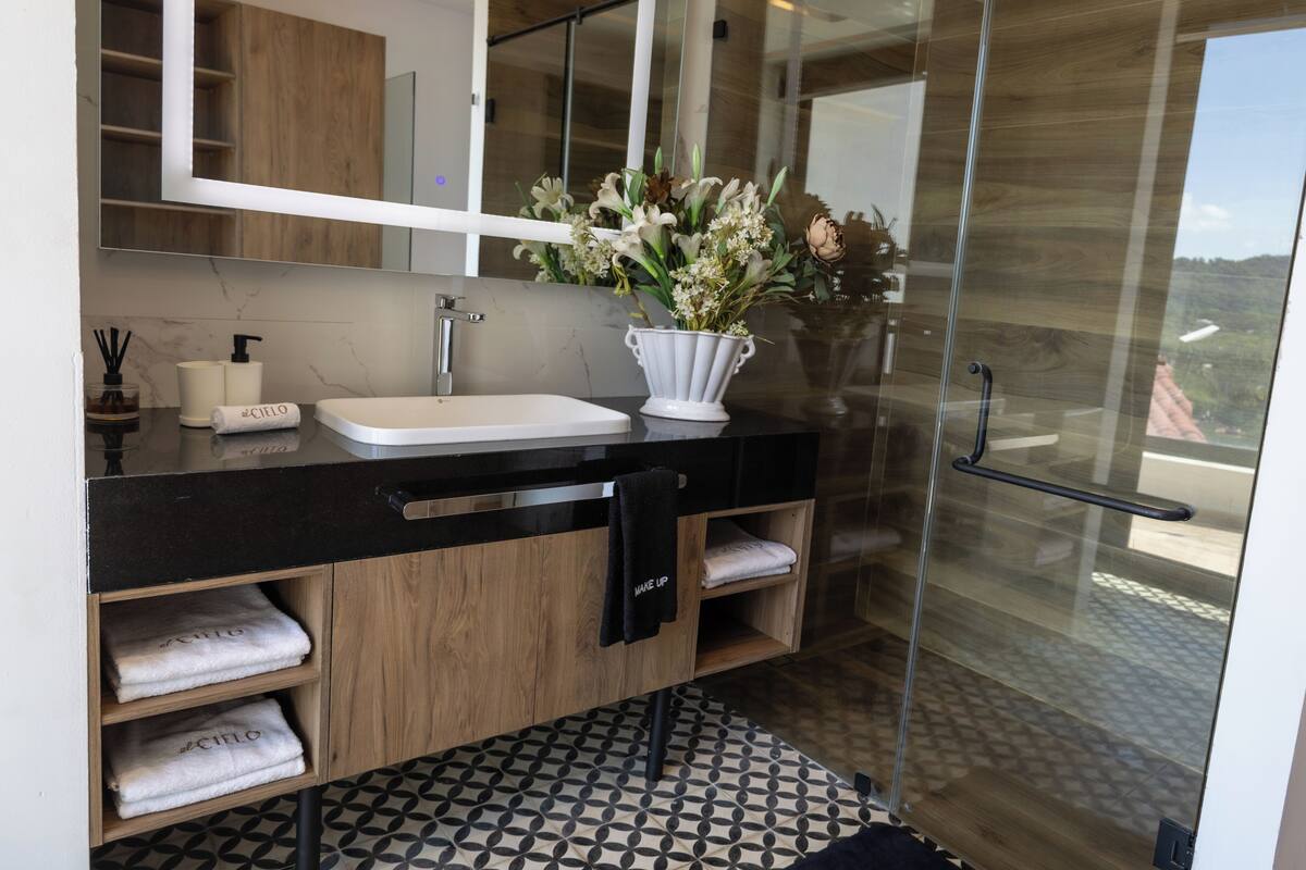 A modern bathroom with a black countertop, white sink, and a glass shower enclosure.