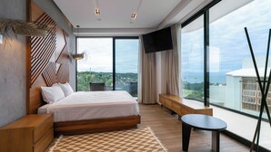 Une chambre moderne avec un grand lit, une petite table ronde, un téléviseur et une vue sur la ville grâce à de grandes fenêtres.